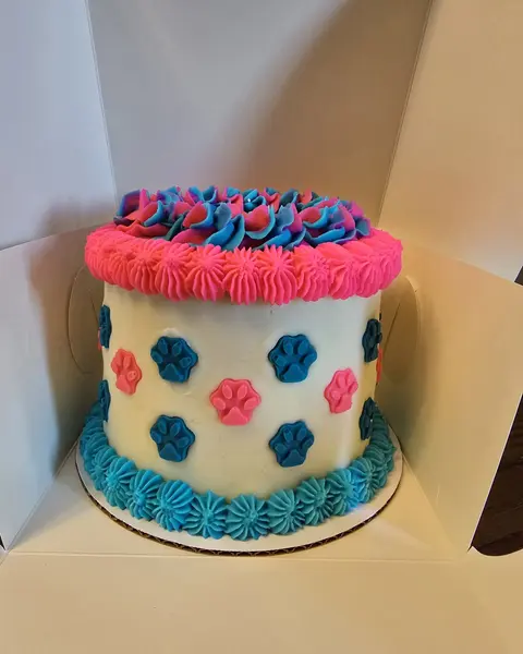 White birthday cake decorated with pink and blue flowers and a blue ruffle border