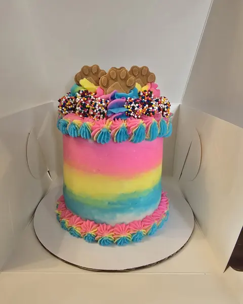 Rainbow-striped birthday cake topped with paw cookies