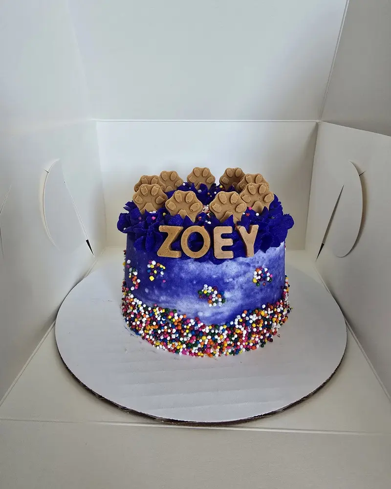 Purple birthday cake with ZOEY piped on it and paw cookies on top